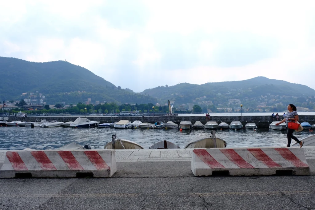 A picture on the boardwalk at lake como, with two concrete blocks with red stripes and a woman with a red bag passing from the right side.